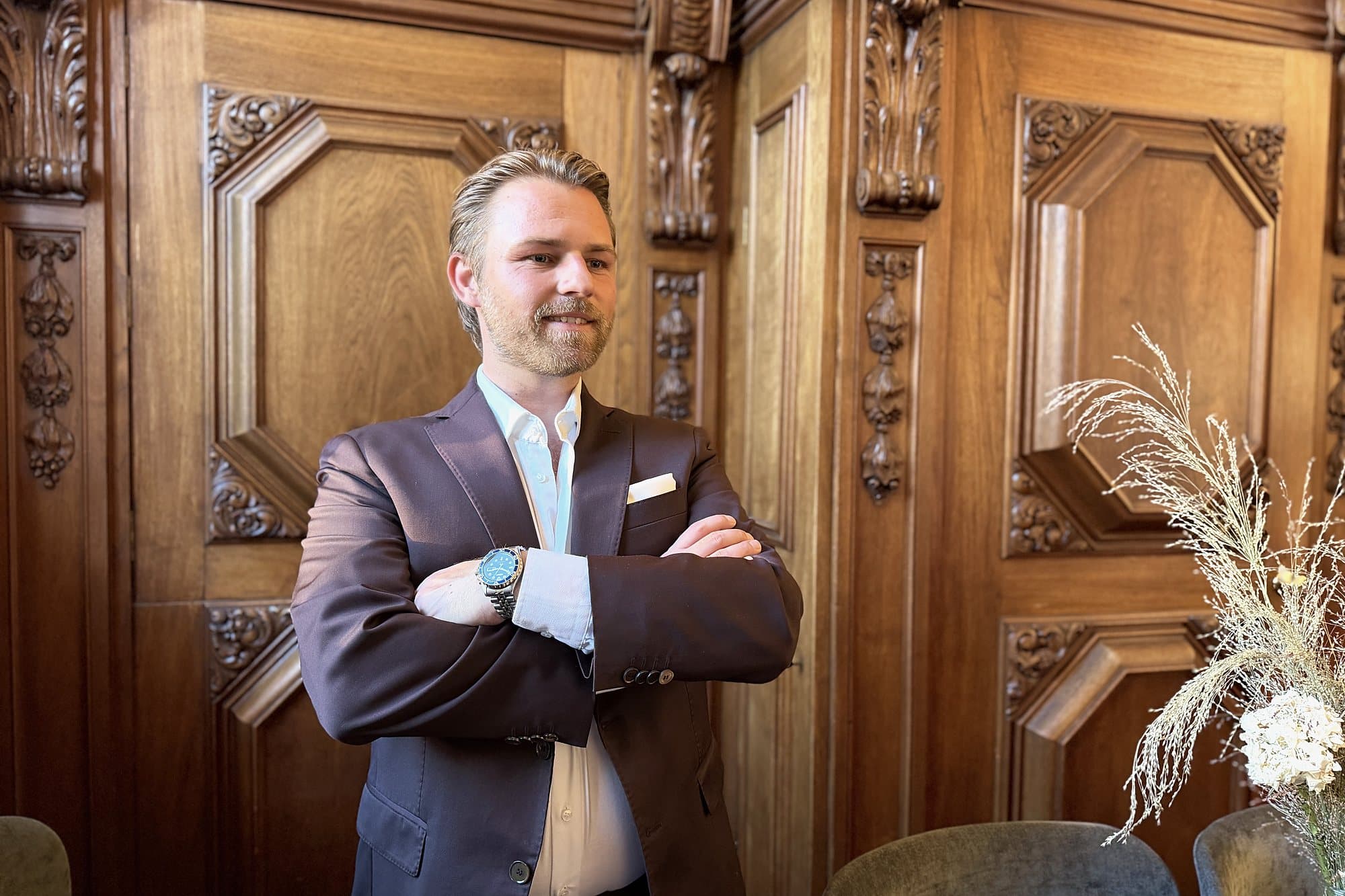 Kim Olsen standing with his arms crossed and a slight smile, in front of carved wooden panelling.