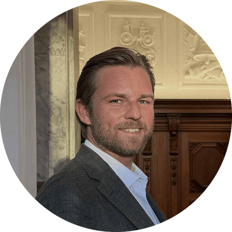 Rundt portræt af Kim Olsen, der smiler, i mørkegrøn jakke og hvid skjorte.
